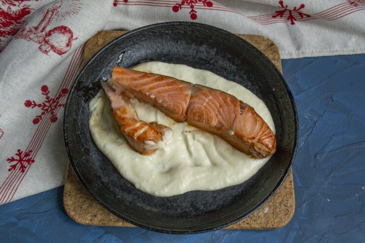Placing the seared trout fillet into the bed of creamy sauce for baking. A seared trout fillet being placed on top of the cream sauce in a skillet.