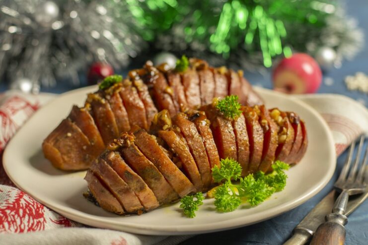 A plate of baked Hasselback sweet potato with a honey and nut glaze, garnished with parsley.