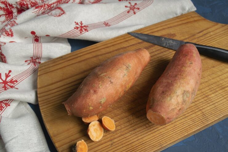 Preparing Sweet Potatoes for Baking Two whole, washed sweet potatoes on a wooden cutting board.