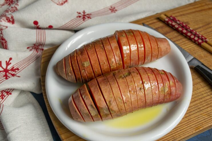 Seasoning the Sweet Potato Before Baking A sliced Hasselback sweet potato being drizzled with olive oil.