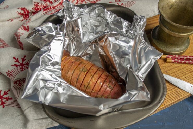 Wrapping Sweet Potatoes in Foil for Baking Two sweet potatoes, each wrapped in aluminum foil, on a baking sheet.