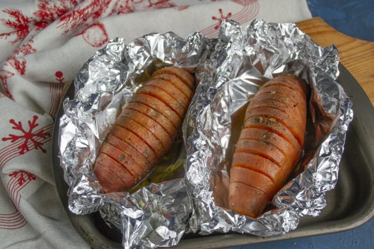 Baking the Sweet Potatoes in the Oven A baking sheet with foil-wrapped sweet potatoes going into an oven.