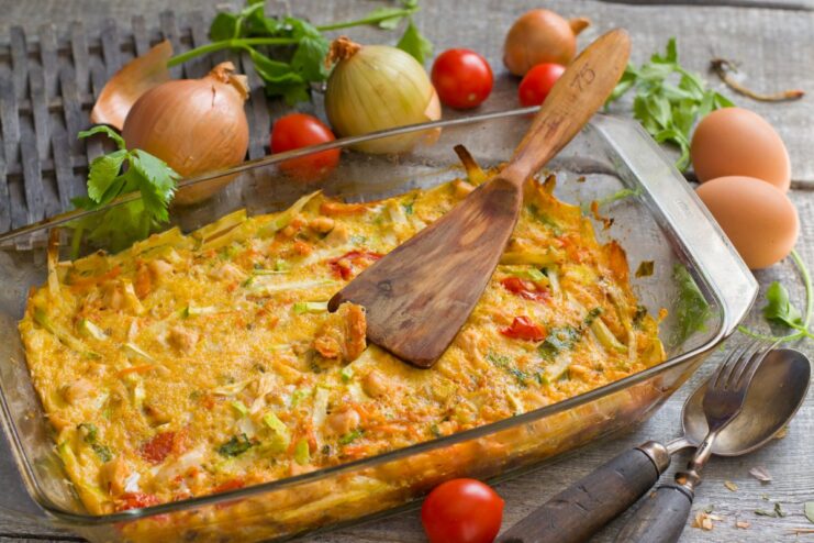 A slice of zucchini and chicken casserole on a white plate, garnished with fresh herbs.