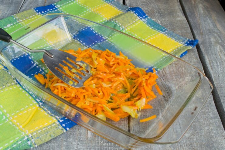 Sautéing Onions and Carrots for the Casserole Base Sautéed onions and carrots in a glass baking dish, forming the first layer of the casserole.
