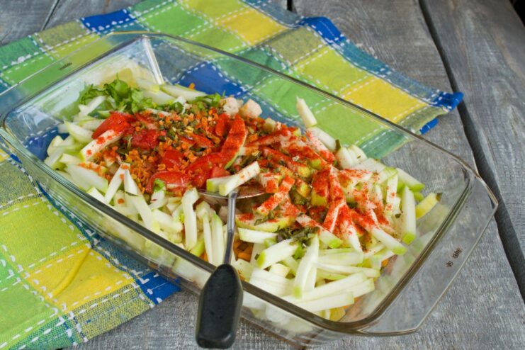 Seasoning the Casserole with Herbs and Spices A mix of vegetables and chicken in a baking dish seasoned with fresh herbs and spices.