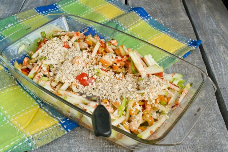 Adding Rolled Oats and Salt to Bind the Casserole Rolled oats and salt being added to the vegetable and chicken mixture in a baking dish.