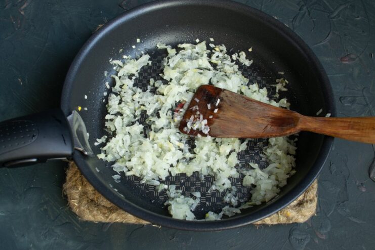 Sautéing Onions Until Translucent for the Casserole Base Chopped onions being sautéed in a frying pan with a wooden spatula.
