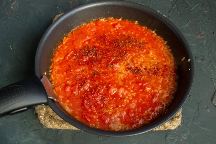 Seasoning the Sauce with Paprika and Red Pepper Spices, including paprika flakes, being added to the tomato sauce in a pan.