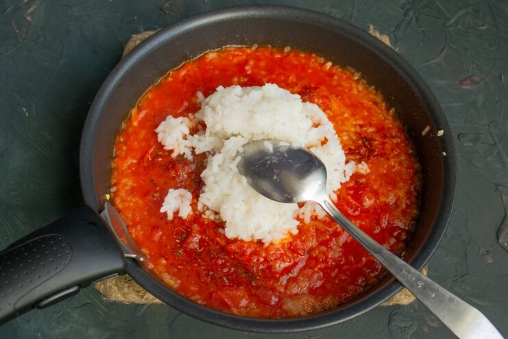 Combining Par-Cooked Rice with the Tomato Sauce Par-cooked white rice being mixed into the tomato sauce in a pan.