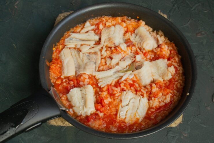 Layering the Poached Pollock Fillet Over the Rice Mixture Poached pollock fillets layered on top of the rice and tomato mixture in a baking dish.