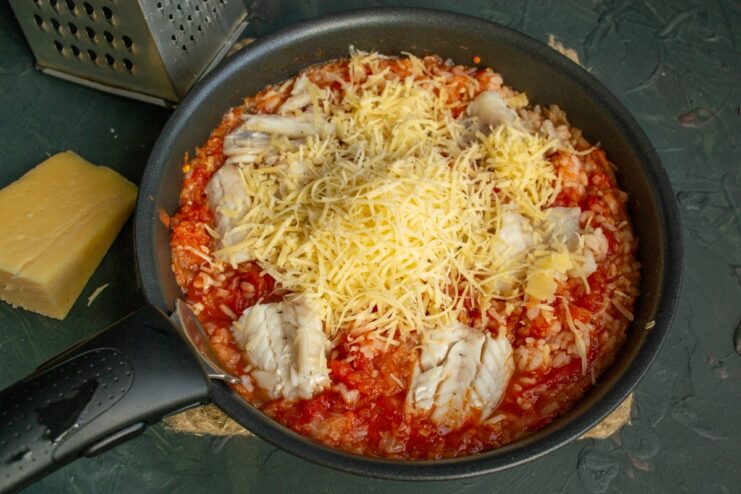 Topping the Casserole with a Generous Layer of Cheese Shredded hard cheese being sprinkled generously over the fish and rice casserole.