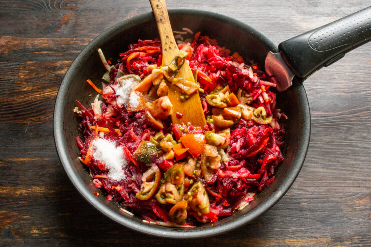 Adding chopped tomatoes to the vegetable mix in the pan. Chopped tomatoes being added to the pan with beets, carrots, and apples.