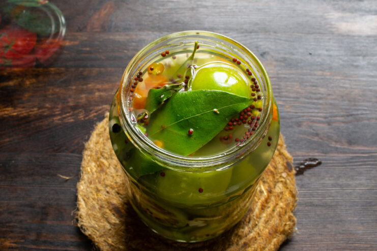 Filling the Jars with Hot Brine - Ensuring Tomatoes are Fully Submerged Hot pickling brine being ladled into a jar of green tomatoes, covering them completely.