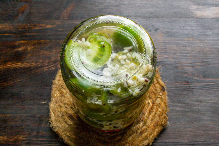 Sealing the Jars - The Final Step Before Pasteurization A hand tightly screwing a metal lid onto a glass jar of pickled green tomatoes.