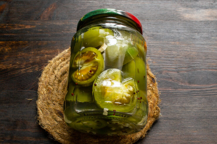 Enjoy Your Homemade Pickles - A Taste of Summer All Winter Long A sealed jar of pickled green tomatoes, ready for storage, with a rustic background.