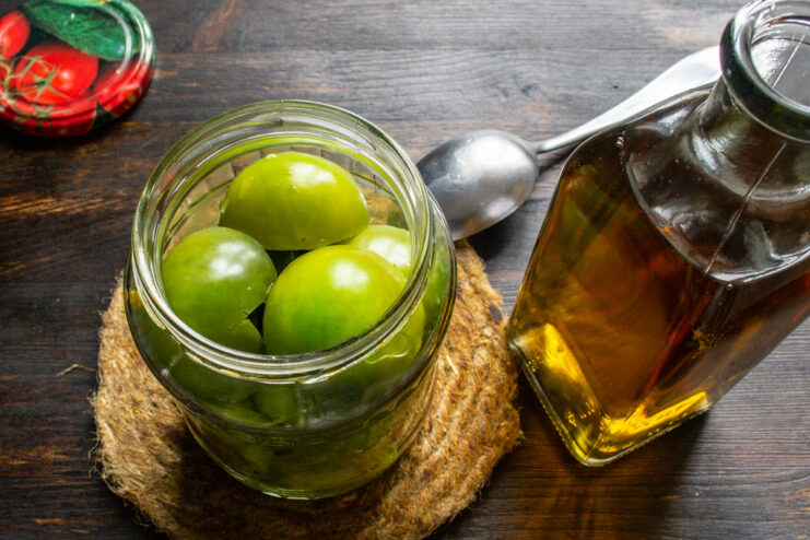 Adding Vinegar to the Jars - Essential for Preservation and Tang Vinegar being poured into glass jars already filled with green tomatoes.