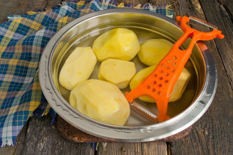 Step 1: Peeling potatoes for the oven-fried recipe A person's hands peeling a large potato over a bowl of water.