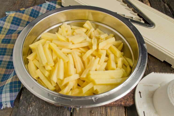 Step 2: Slicing potatoes evenly for consistent cooking A hand using a mandoline slicer to cut a potato into thin, even slices.