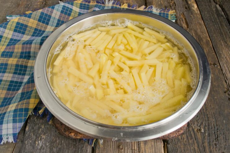 Step 3: Rinsing starch off the potato slices Sliced potatoes in a metal colander being rinsed under running water.