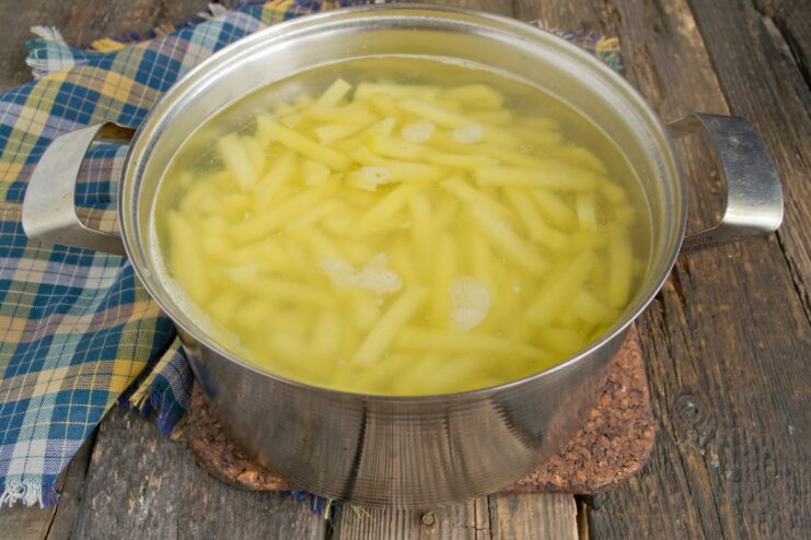 Step 4: Parboiling the potato slices Sliced potatoes being added from a colander into a pot of boiling water.