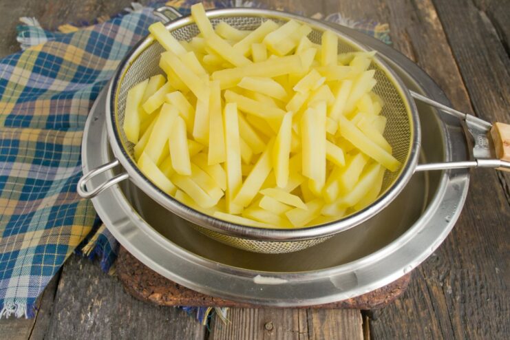 Step 5: Draining the parboiled potatoes Parboiled potato slices being drained in a metal colander in a sink.