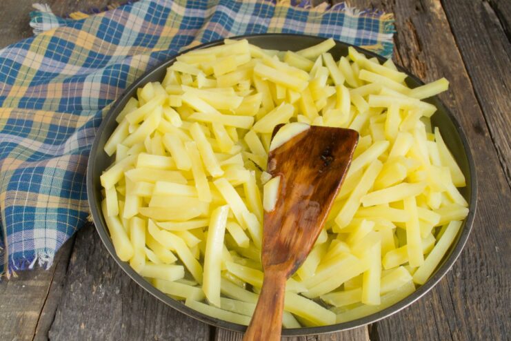 Step 7: Adding potatoes to the hot oil Parboiled potato slices being carefully added to a hot skillet with oil.
