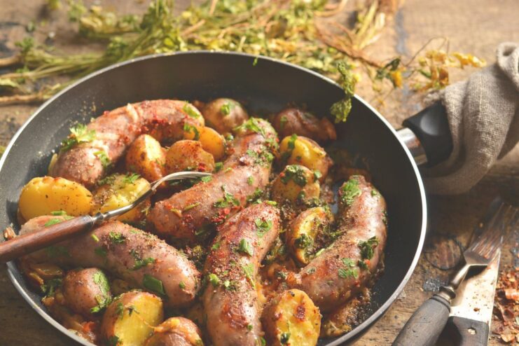 A skillet filled with rustic fried sausage and potatoes, garnished with fresh herbs.