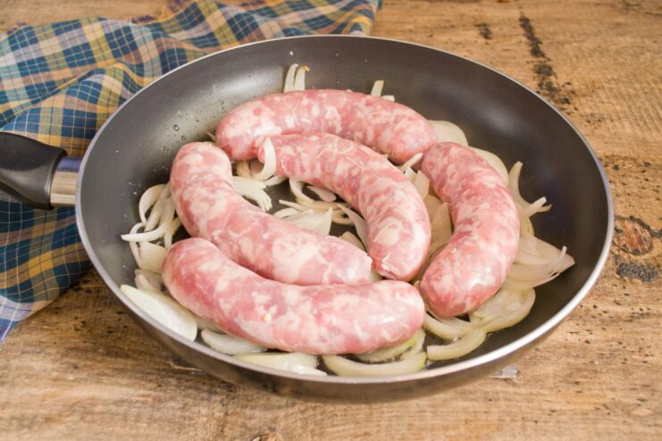 Browning the Sausages for a Perfect Crust Pork sausages browning in a skillet with sautéed onions.