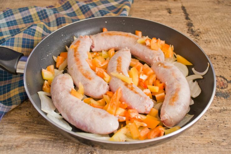 Adding Bell Peppers for Sweetness and Color Diced bell peppers being added to the skillet with sausages and onions.