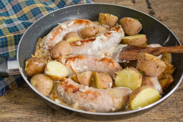 Tossing in Cooked Potatoes to Complete the Dish Cooked potato wedges being added to the skillet with sausage and creamy sauce.