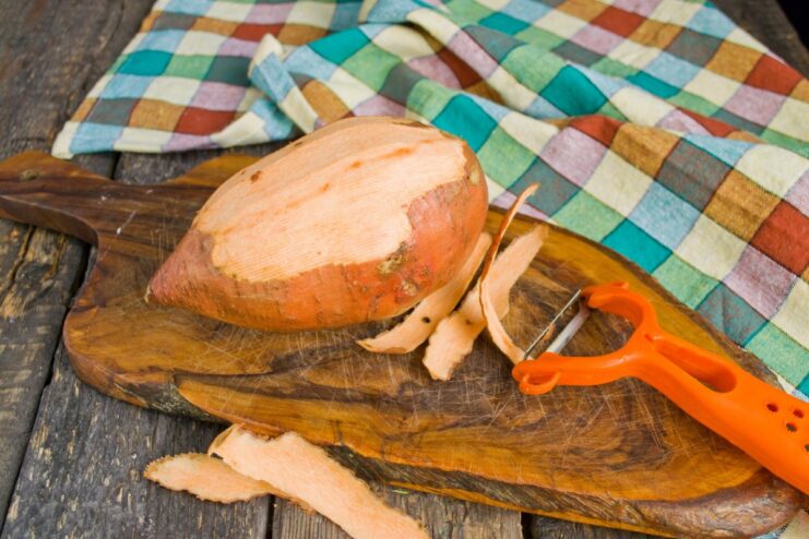 Step 1: Peeling the Sweet Potato Skin A person using a vegetable peeler to remove the skin from a large sweet potato tuber.