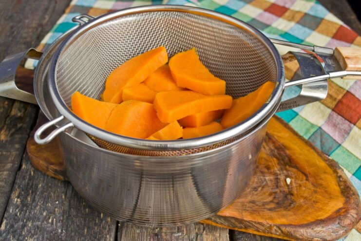 Draining the Parboiled Sweet Potatoes Parboiled sweet potato slices being drained in a metal sieve over a bowl.