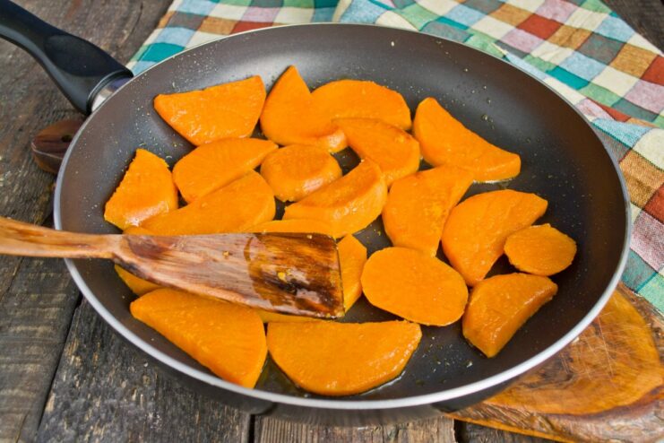 Frying Sweet Potato Slices Until Golden Sweet potato slices frying in a pan, turning golden-brown on one side.