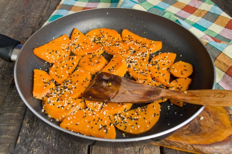 Seasoning the Fried Sweet Potatoes Fried sweet potato slices in a pan being sprinkled with sesame seeds and red pepper.