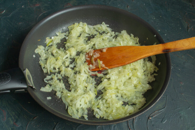 Sautéing Onions for the Zrazy Filling Finely chopped onions being sautéed in a frying pan until soft and translucent.