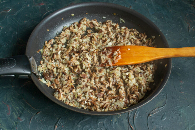 Cooking the Savory Mushroom and Onion Filling Chopped honey mushrooms being added to sautéed onions in a pan to make the zrazy filling.