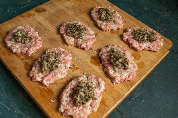 Adding the Mushroom Filling to the Meat Patties Mushroom and onion filling being placed in the center of a flattened minced meat patty.