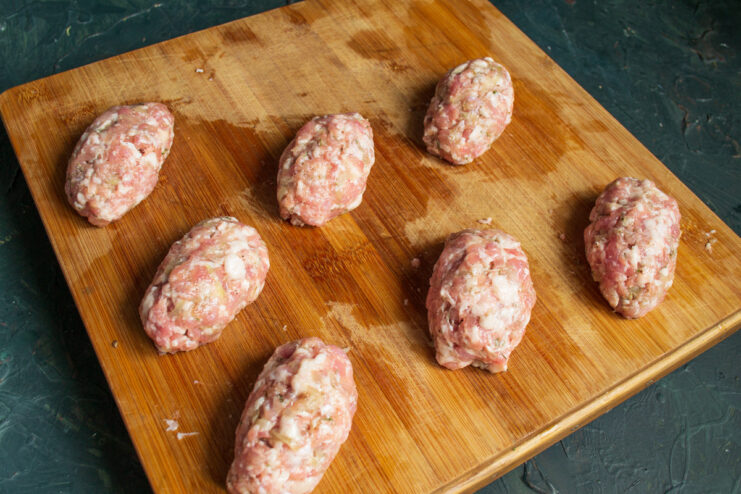 Shaping the Stuffed Meat Zrazy Hands shaping a raw meat patty stuffed with mushroom filling into an oval zrazy.