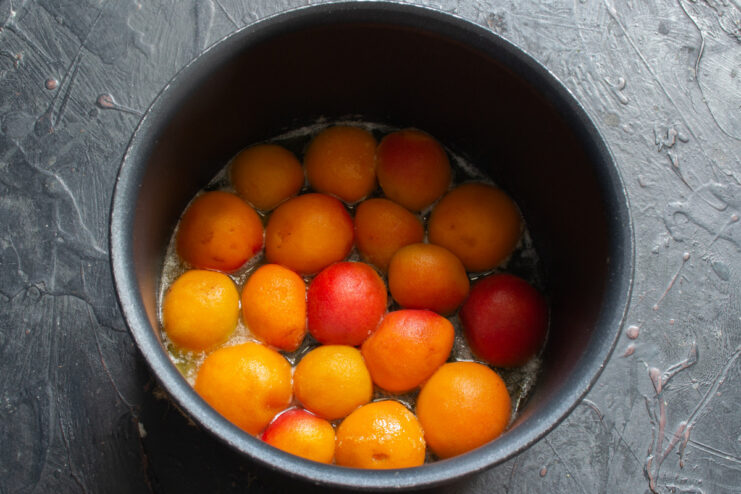 Arranging apricot halves in the caramel for the cake base Apricot halves arranged cut-side down in a skillet with bubbling caramel sauce.