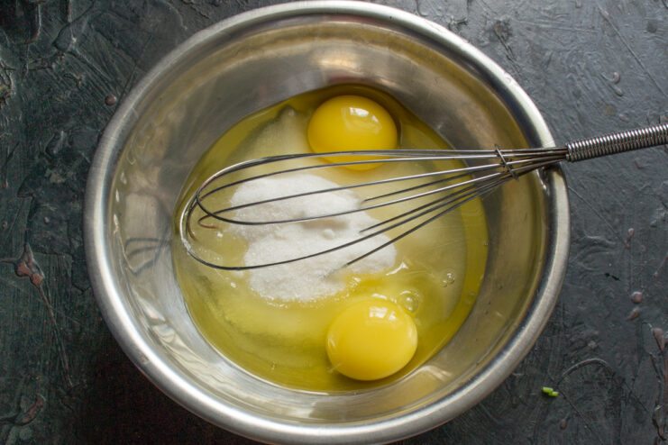 Starting the cake batter by combining sugar and eggs A glass bowl containing granulated sugar and two cracked eggs, ready for mixing.