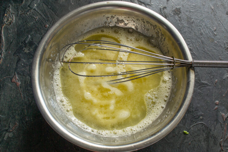 Mixing wet ingredients for the cake batter Melted butter being poured into a bowl with a whisked egg and sugar mixture.