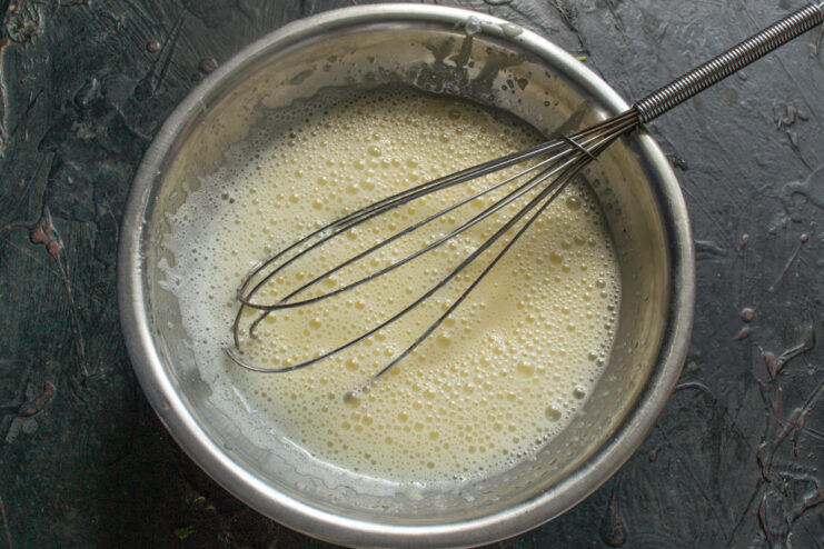 Combining all the wet ingredients for a smooth batter A hand mixer blending the wet ingredients for the cake batter in a glass bowl.