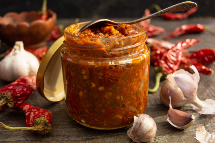 A glass jar filled with vibrant red dried chili pepper adjika, ready for storage.