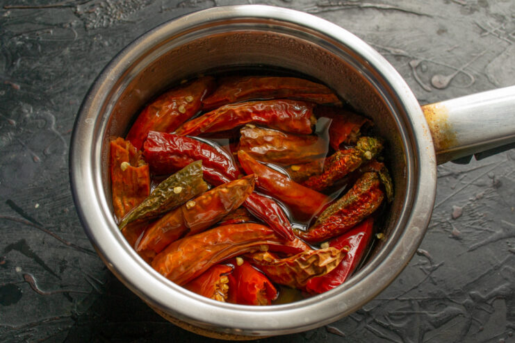 Step 1: Soaking Dried Chili Peppers in Water Dried red chili peppers in a metal saucepan, being covered with water to rehydrate.