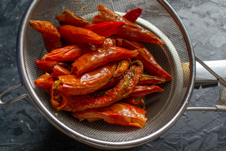 Step 2: Draining the Soaked Chili Peppers Rehydrated red chili peppers draining in a metal sieve over a bowl.