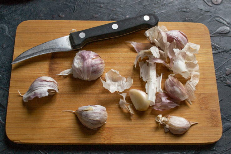 Preparing the Garlic for the Adjika Fresh garlic cloves separated from the bulb on a wooden cutting board.