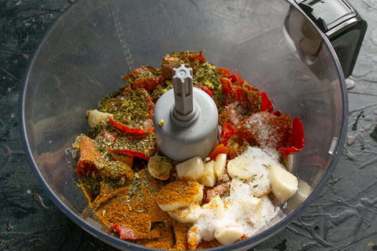 Adding Herbs and Spices to the Chili Mixture Dried herbs and spices being added to the chili and garlic mixture in a blender.