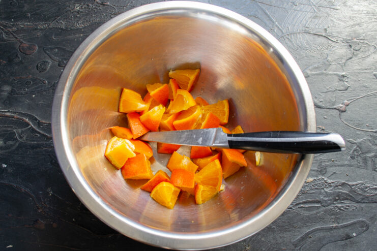 Preparing the orange for the mannik batter by dicing it with the peel on for maximum flavor. A whole orange being diced into small cubes on a cutting board.