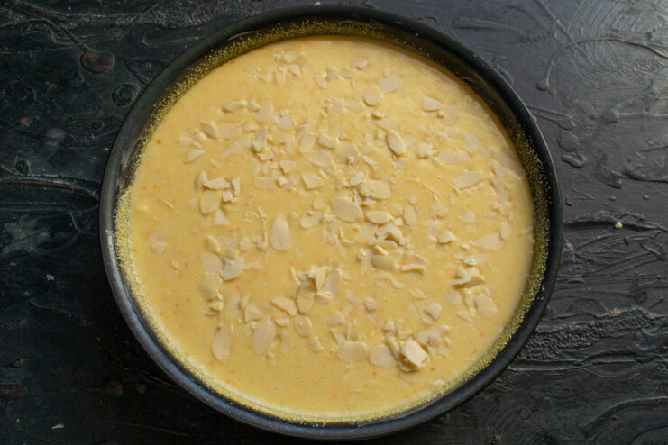 The final step before baking: pouring the rested semolina batter into the pan. The orange semolina cake batter being poured into a buttered and polenta-dusted pan.