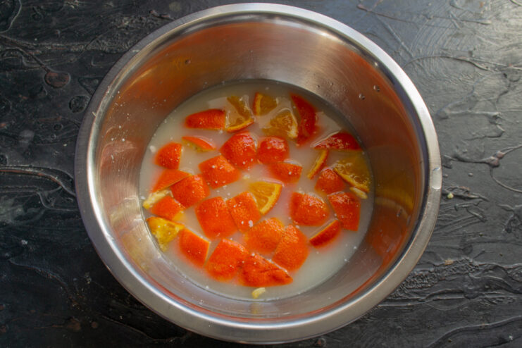 Adding whey to the diced orange, a key step for a moist semolina cake. Milk whey being poured from a glass into a bowl containing diced orange.